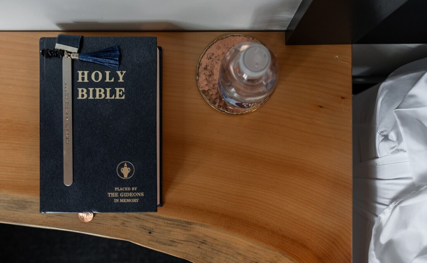 Una Biblia sobre una superficie de madera, con un separador metálico y un vaso de agua.