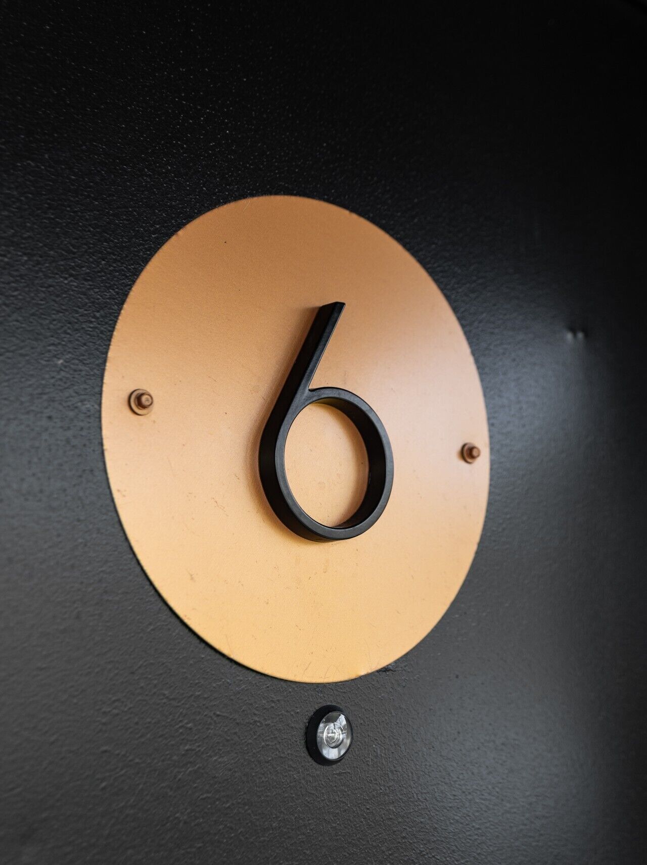 A metallic number '6' on a circular plaque, mounted on a wall.