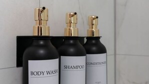 Three bottles of body wash, shampoo, and conditioner mounted on a black wall.