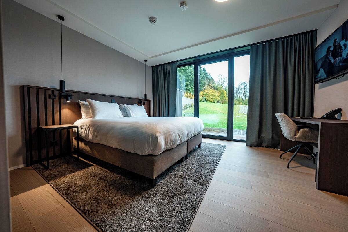 Une chambre d’hôtel moderne, dotée d’un grand lit, d’un bureau et offrant une vue sur l’extérieur.