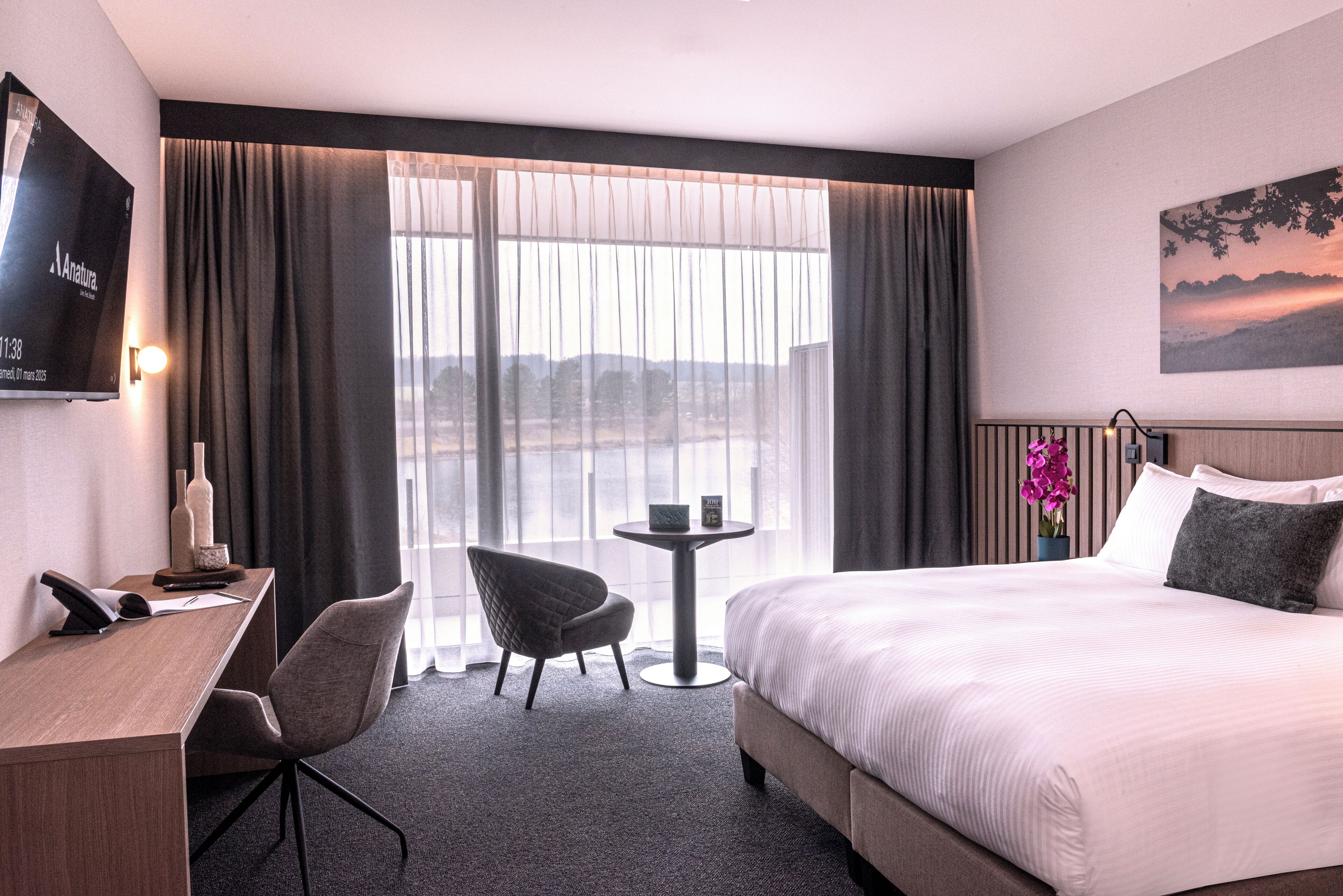 Een hotelkamer met een bed, een bureau met telefoon, een stoel, een kleine tafel en een aan de muur bevestigde televisie.
