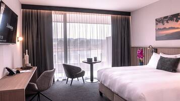 Een hotelkamer met een bed, een bureau met telefoon, een stoel, een kleine tafel en een aan de muur bevestigde televisie.