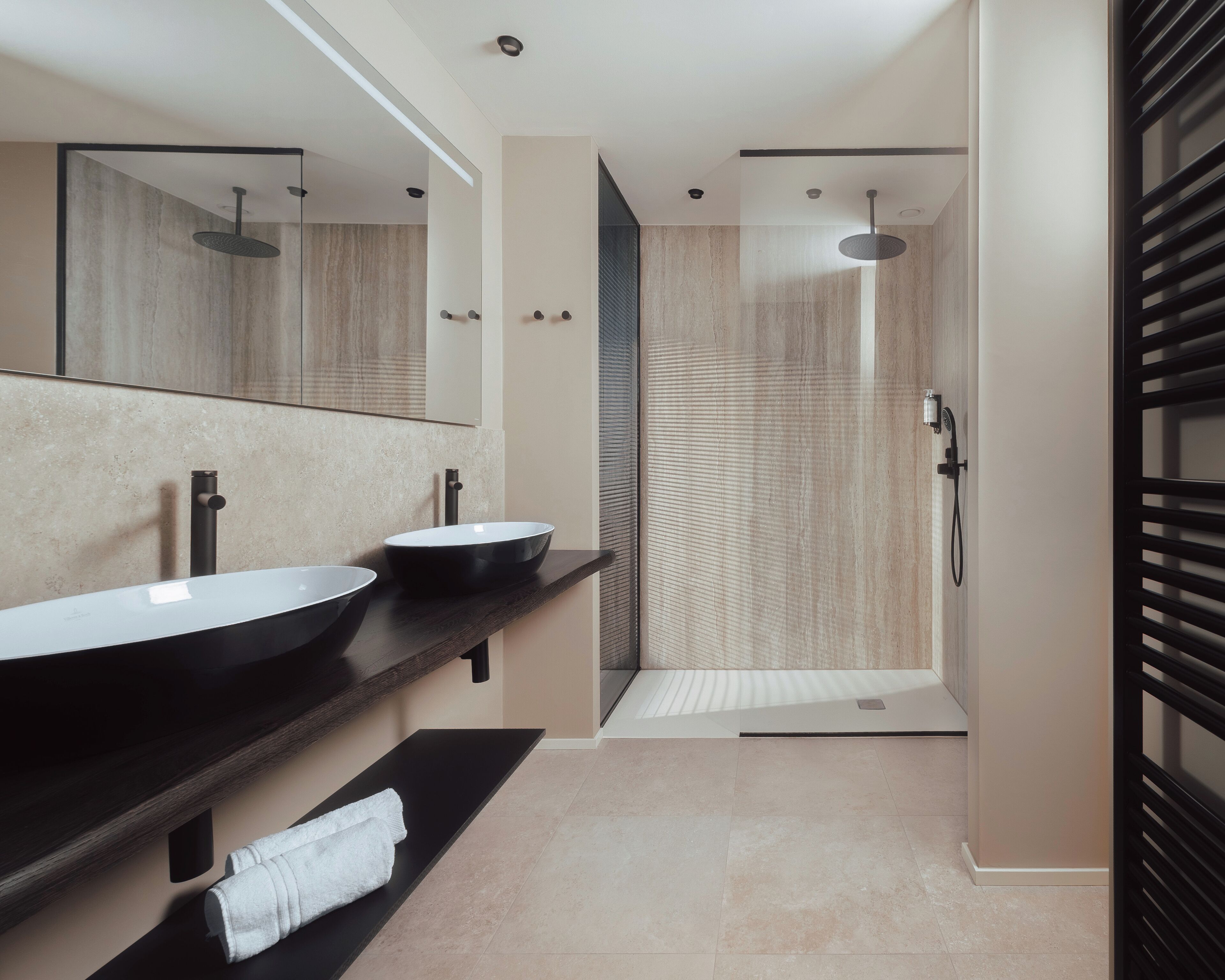 A modern bathroom with two sinks, a shower, and a large mirror.