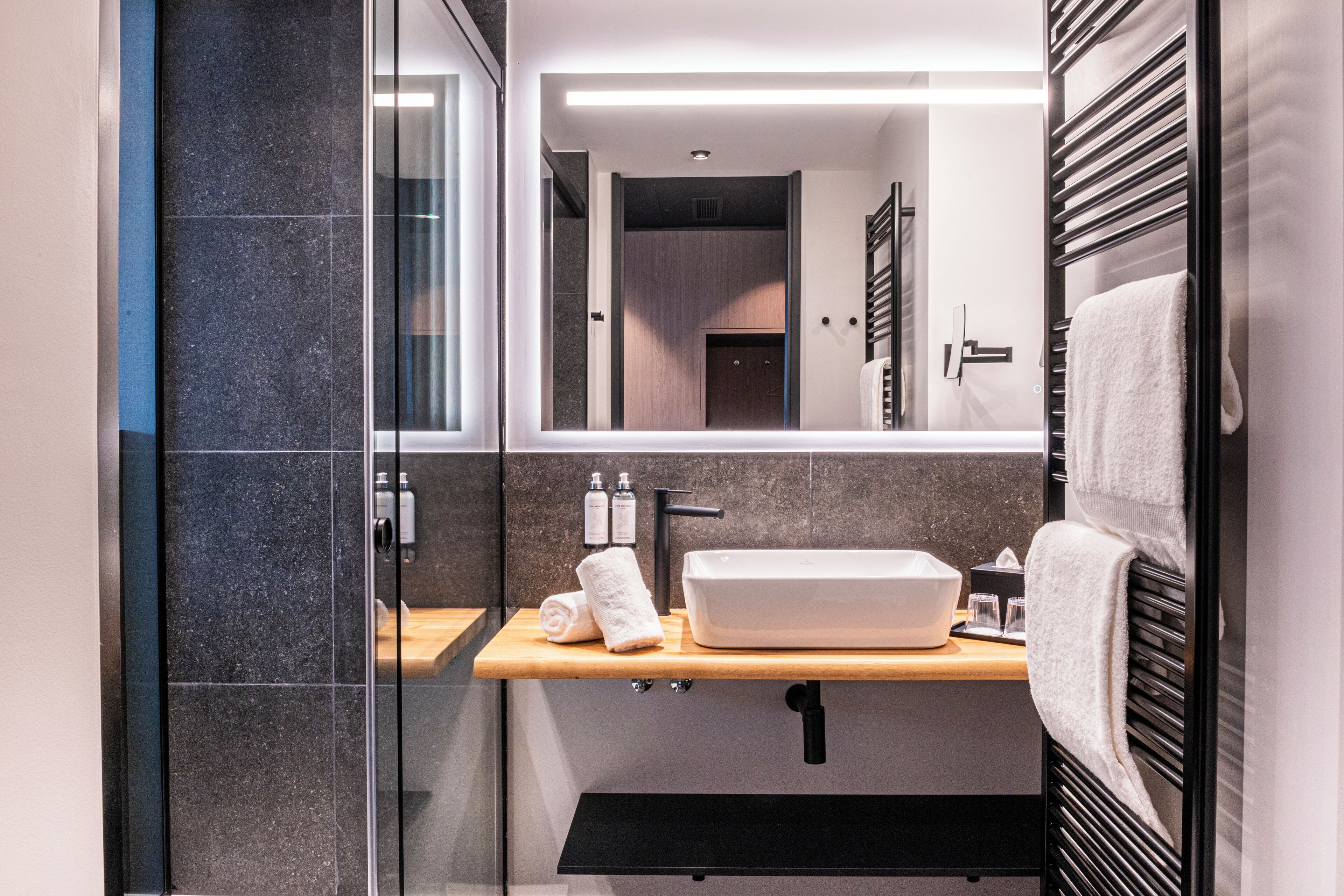 Une salle de bain moderne avec une douche à parois de verre, un meuble-lavabo en bois avec un évier blanc et un porte-serviettes.