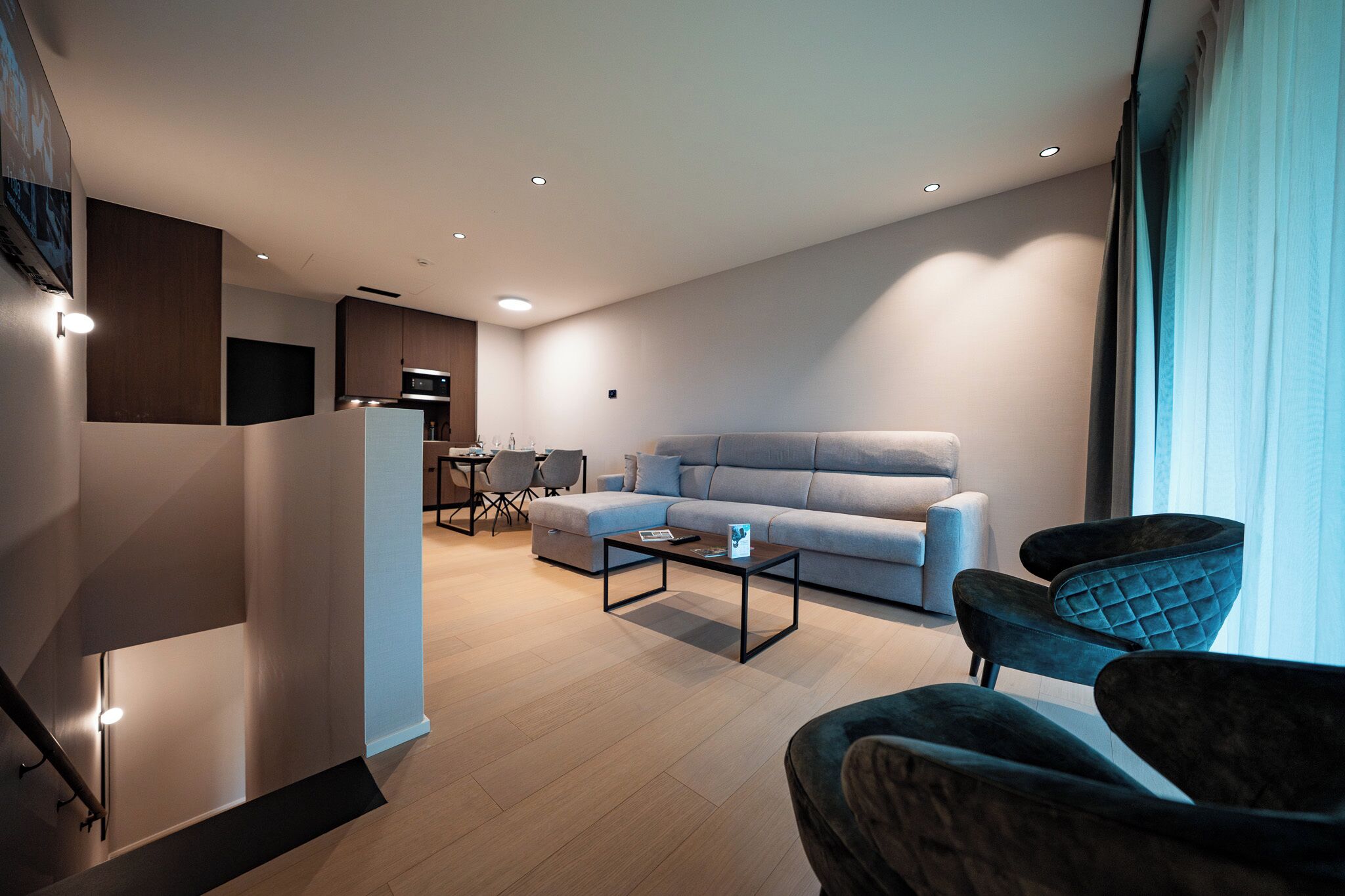 Un salon moderne avec un canapé, une table basse et deux fauteuils. On aperçoit à l’arrière-plan un coin repas avec une table et des chaises.