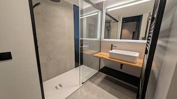 Een moderne badkamer met een douchecabine van glas, een witte wasbak op een houten plank en een spiegel erboven.