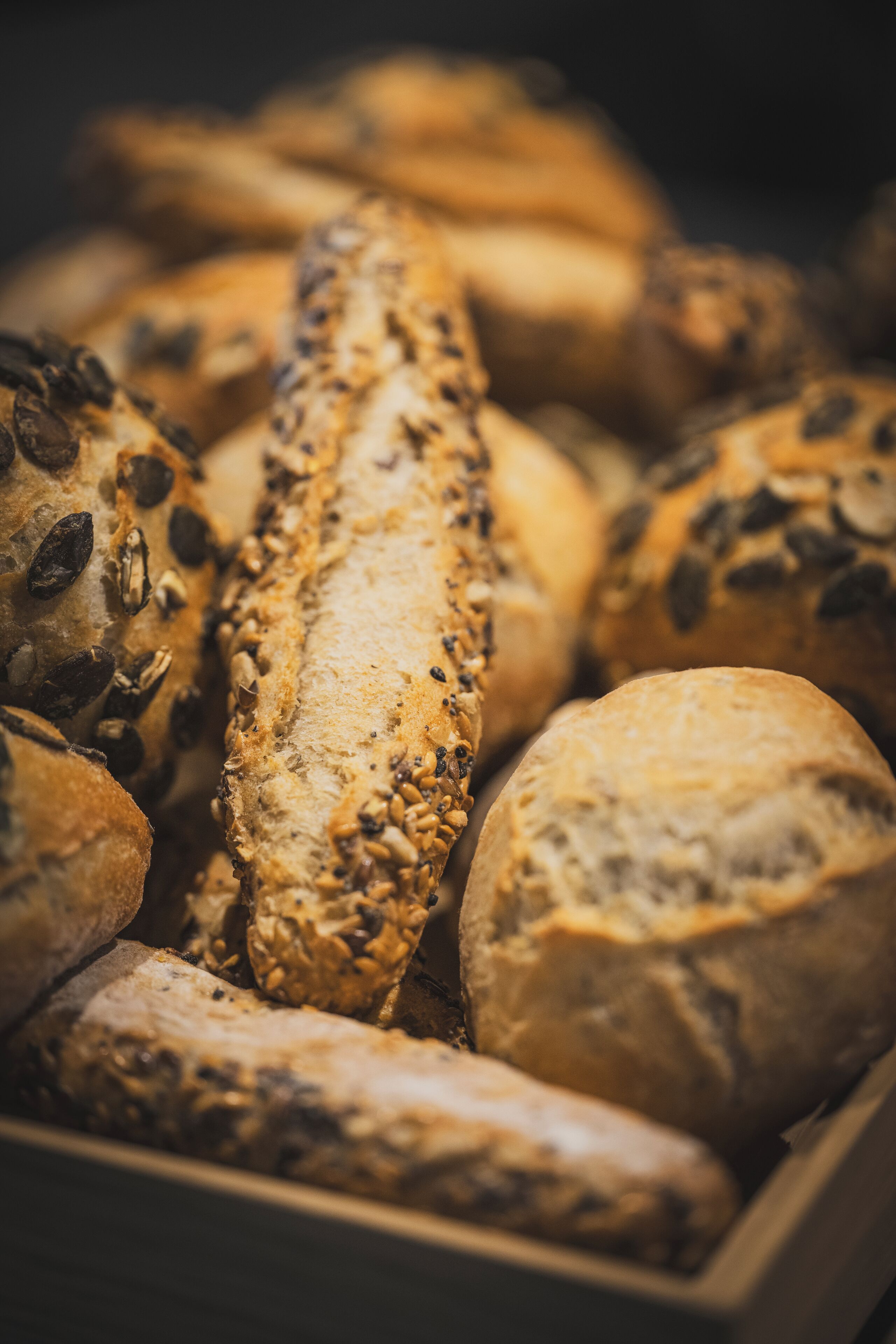 Verschiedene Brotsorten mit Saaten und Getreide, präsentiert in einem Holzkasten.
