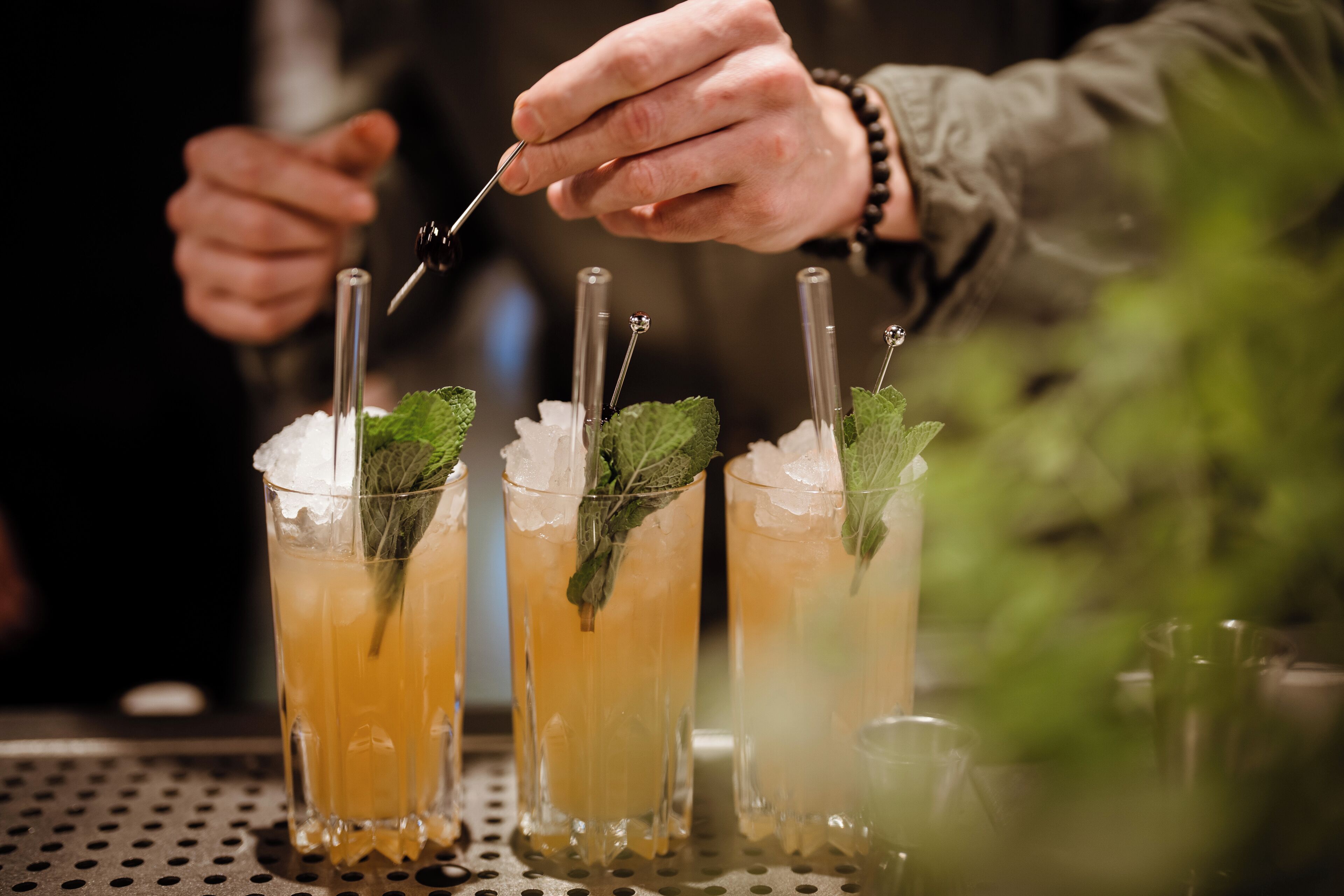 A bartender preparing drinks with straws and mint leaves.