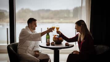 A couple toasting with champagne glasses at a round table with a view of a lake.