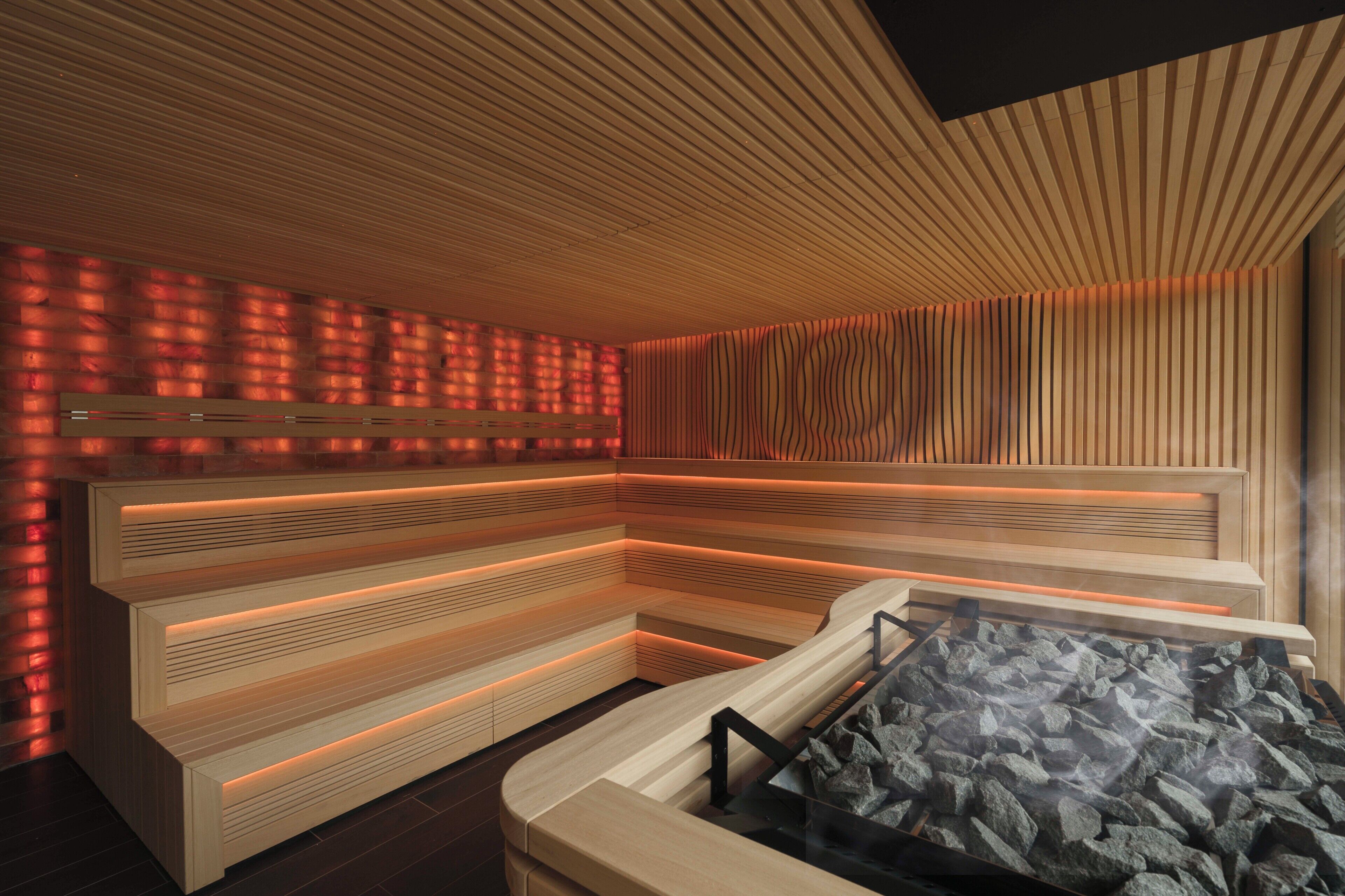 Een moderne sauna met houten banken en een glazen tafel, een wand met een structuurpatroon en een plafond met een gesloten lambrisering.