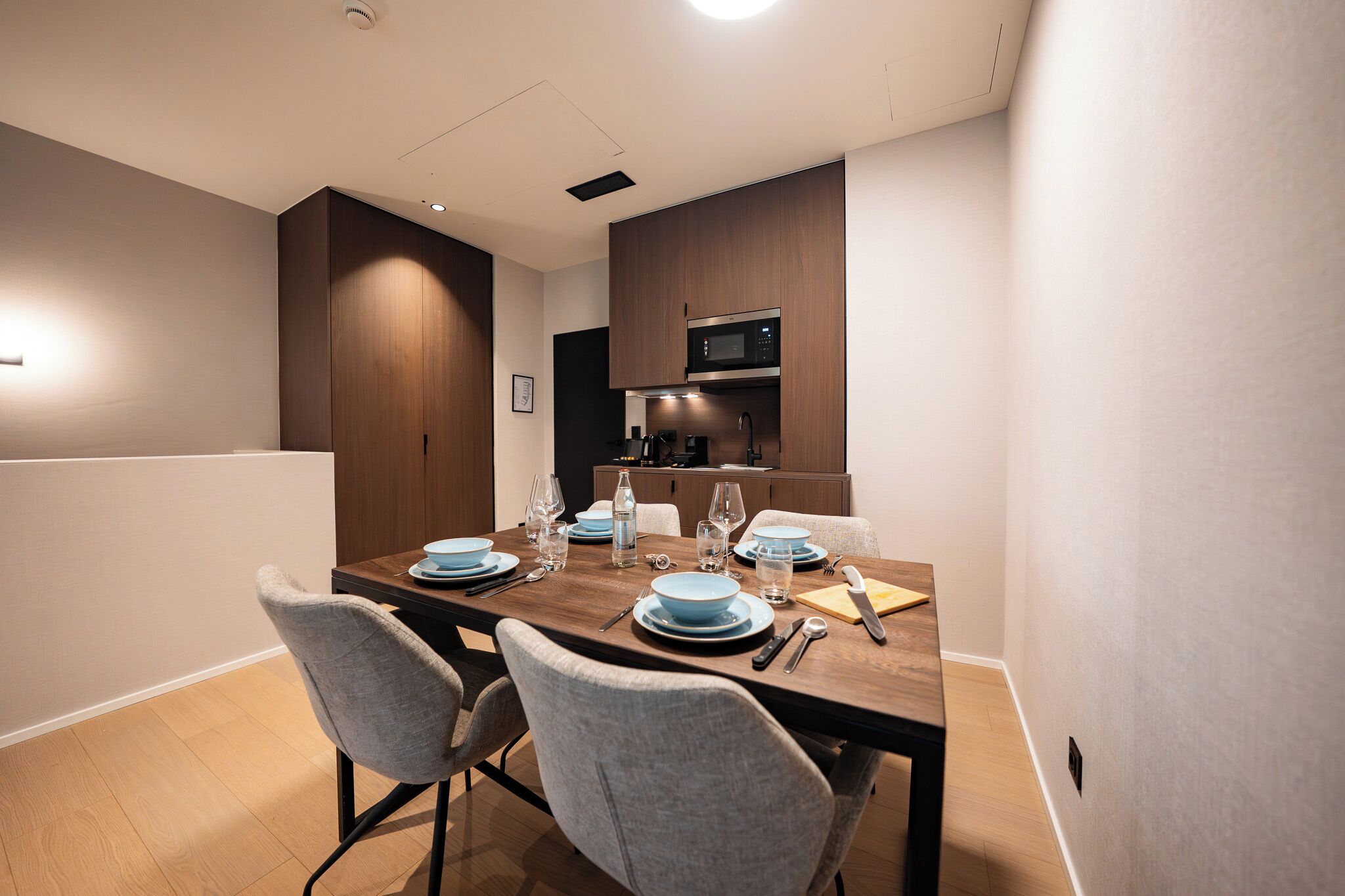 Un espace de salle à manger moderne avec une table en bois dressée pour quatre personnes, agrémentée d’assiettes, de verres et de couverts.