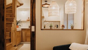 A cozy living room with a dark sofa, a round table with a book and a candle, wooden flooring, and a staircase leading to another room. - La Tanière - Nature and relaxation gîte (Durbuy)