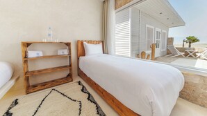 A bedroom with a large bed, a wooden shelf with towels, and a view of the beach. - New Spirit Dakhla (Dakhla)