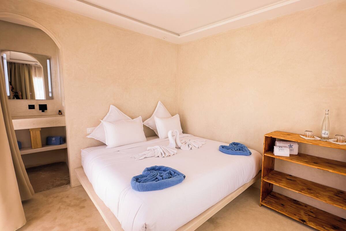 A hotel room with a large bed, a wooden shelf with towels, and a mirror.