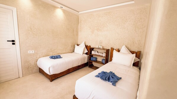 A hotel room with two beds, a wooden nightstand, and a beige textured wall. - New Spirit Dakhla (Dakhla)