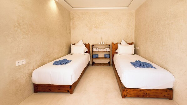 A twin room with two beds, a wooden headboard, a nightstand, and a small shelf with towels. - New Spirit Dakhla (Dakhla)