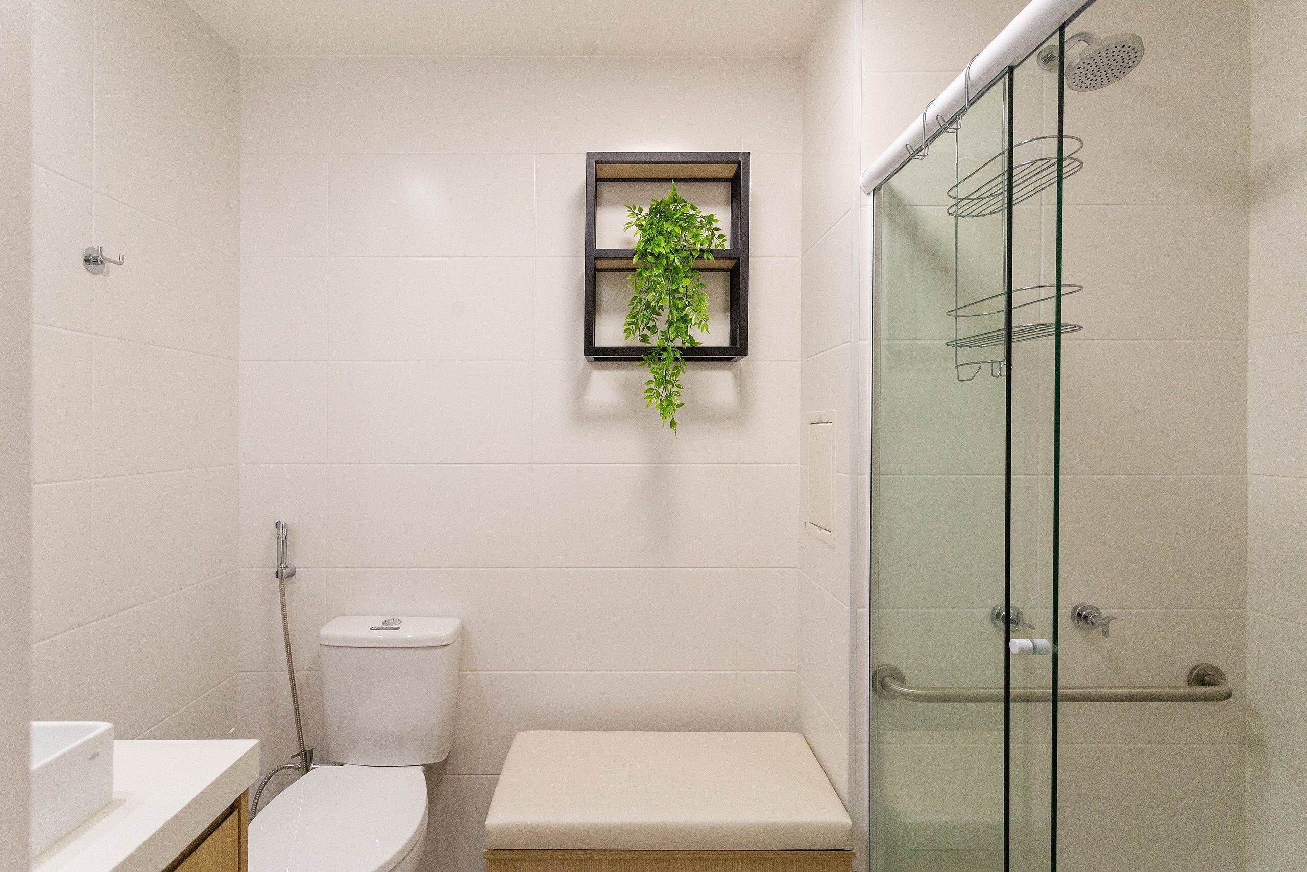 Et badeværelse med toilet, bænk, brusekabine i glas og en hylde med en plante.