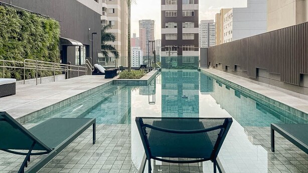 Une piscine sur le toit, agrémentée de chaises longues, entourée de bâtiments modernes et de palmiers.
