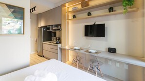 Une chambre d’hôtel moderne équipée d’un lit, d’une petite kitchenette, d’une télévision et d’une plante.