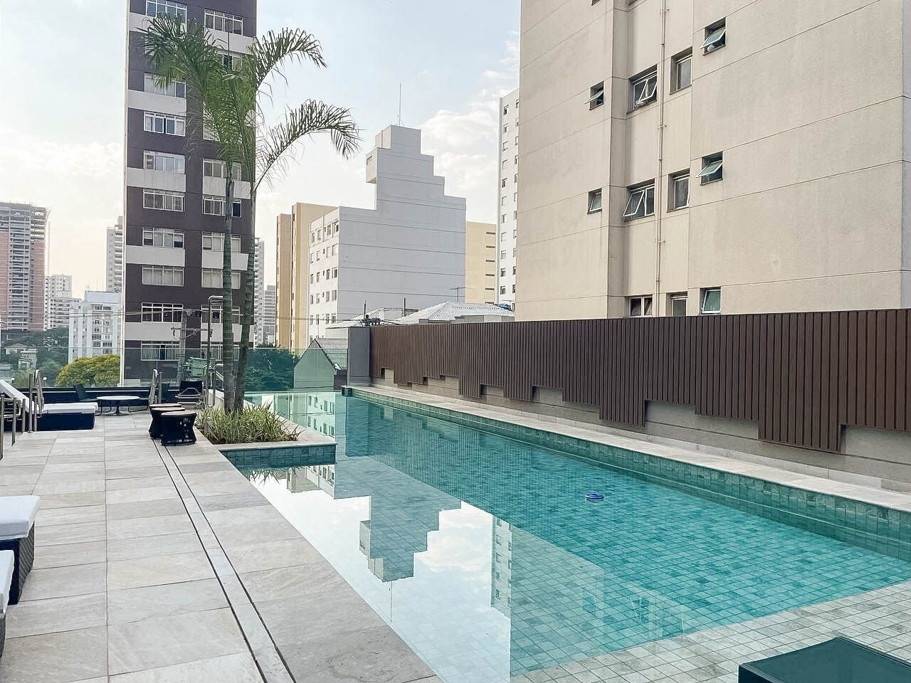 Ein Pool auf dem Dach mit freiem Blick auf die umliegenden Gebäude, einer Palme und Sitzgelegenheiten im Freien.