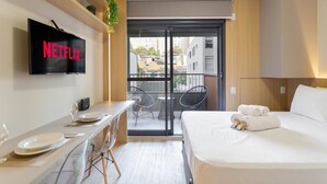Une chambre d’hôtel moderne dotée d’un téléviseur à écran plat affichant « NETFLIX », d’un balcon avec des chaises et d’un lit soigneusement fait avec des serviettes.