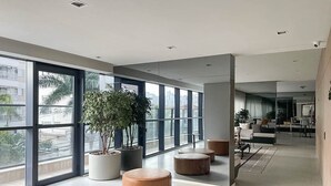 Un hall d’entrée spacieux, doté de grandes fenêtres, d’espaces de détente aménagés avec des sièges circulaires et de plantes en pot.