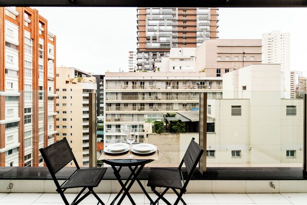 A balcony with a table set for two, overlooking a cityscape with multiple buildings.