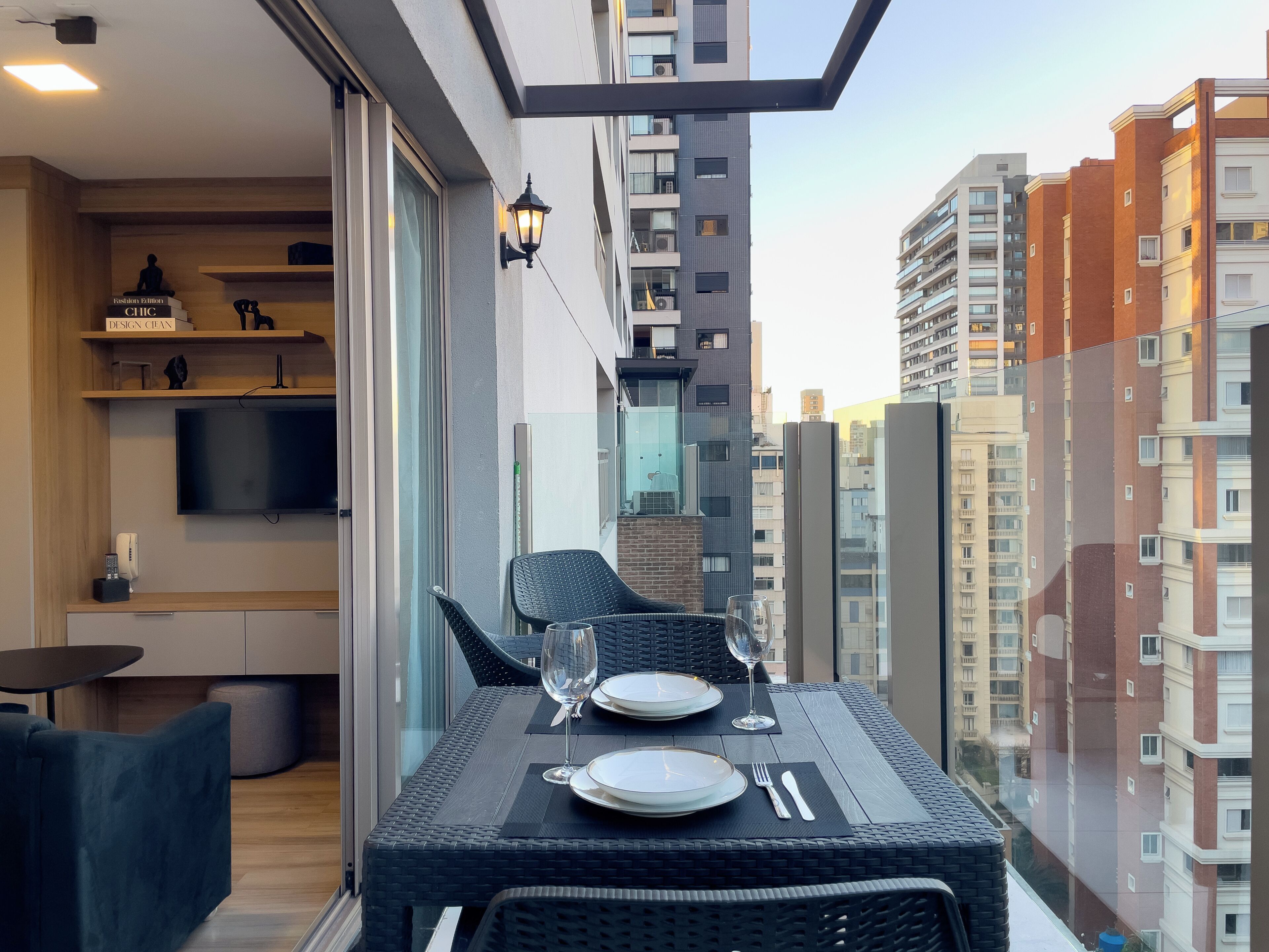 Ein Balkon mit Esstisch für zwei Personen, einem an der Wand befestigten Fernseher und Blick auf die Stadt.