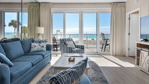 Una sala de estar moderna con un sofá azul, una mesa de centro y vistas a la playa a través de amplios ventanales.