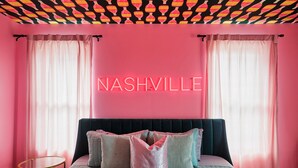 A pink-themed bedroom with a neon sign reading "NASHVILLE," a bed with multiple pillows, and sheer curtains. - Ultimate Bach 10min to DT, Insta Walls Every Room (Nashville)