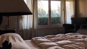 Une chambre à coucher avec un lit, une chaise, une lampe et une fenêtre avec des rideaux.