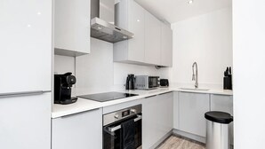 A modern kitchen with white cabinets, a stainless steel range hood, a built-in oven, a microwave, and a coffee maker.
