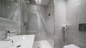 A modern bathroom with a glass-enclosed shower, a white sink, and a toilet.