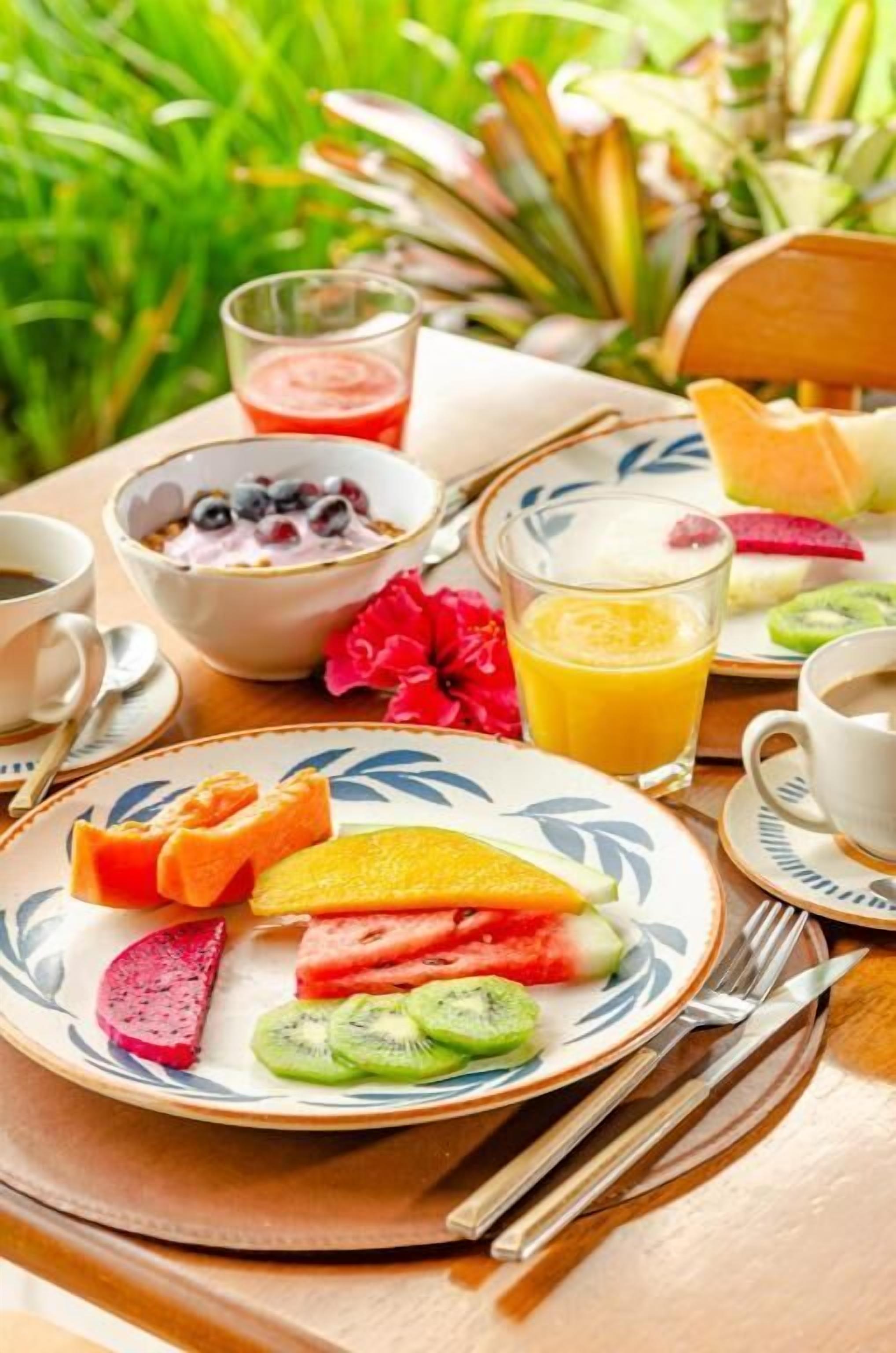 A breakfast setting with a plate of fruit, a bowl of yogurt with berries, a glass of orange juice, and a cup of coffee.
