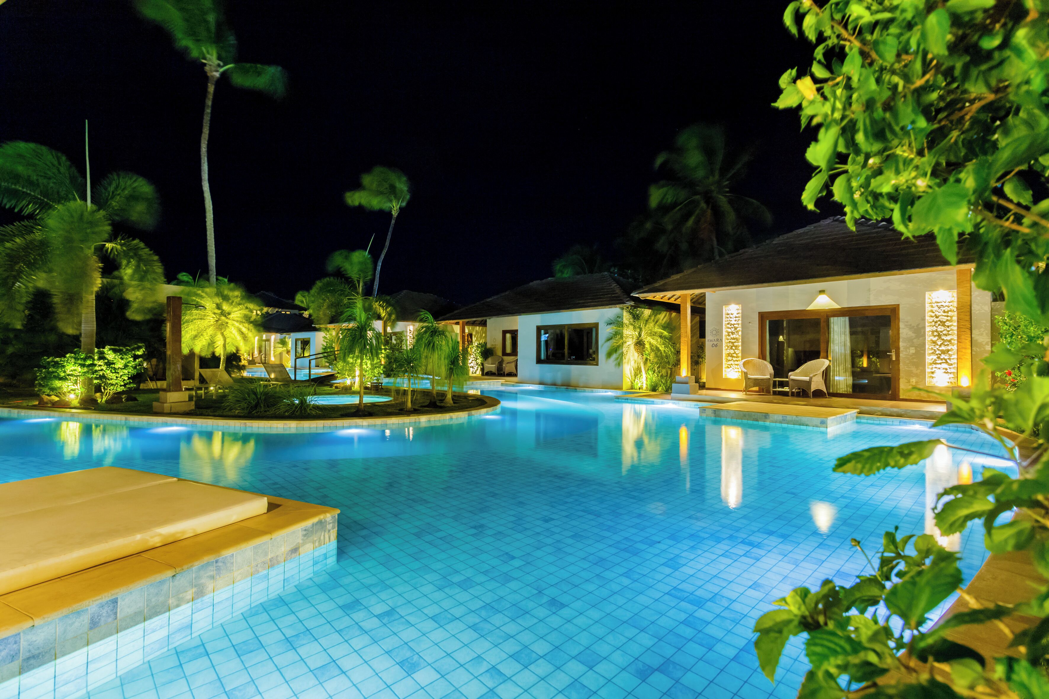 A swimming pool surrounded by palm trees and a building with a covered patio area.