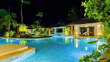 A swimming pool surrounded by palm trees and a building with a covered patio area.
