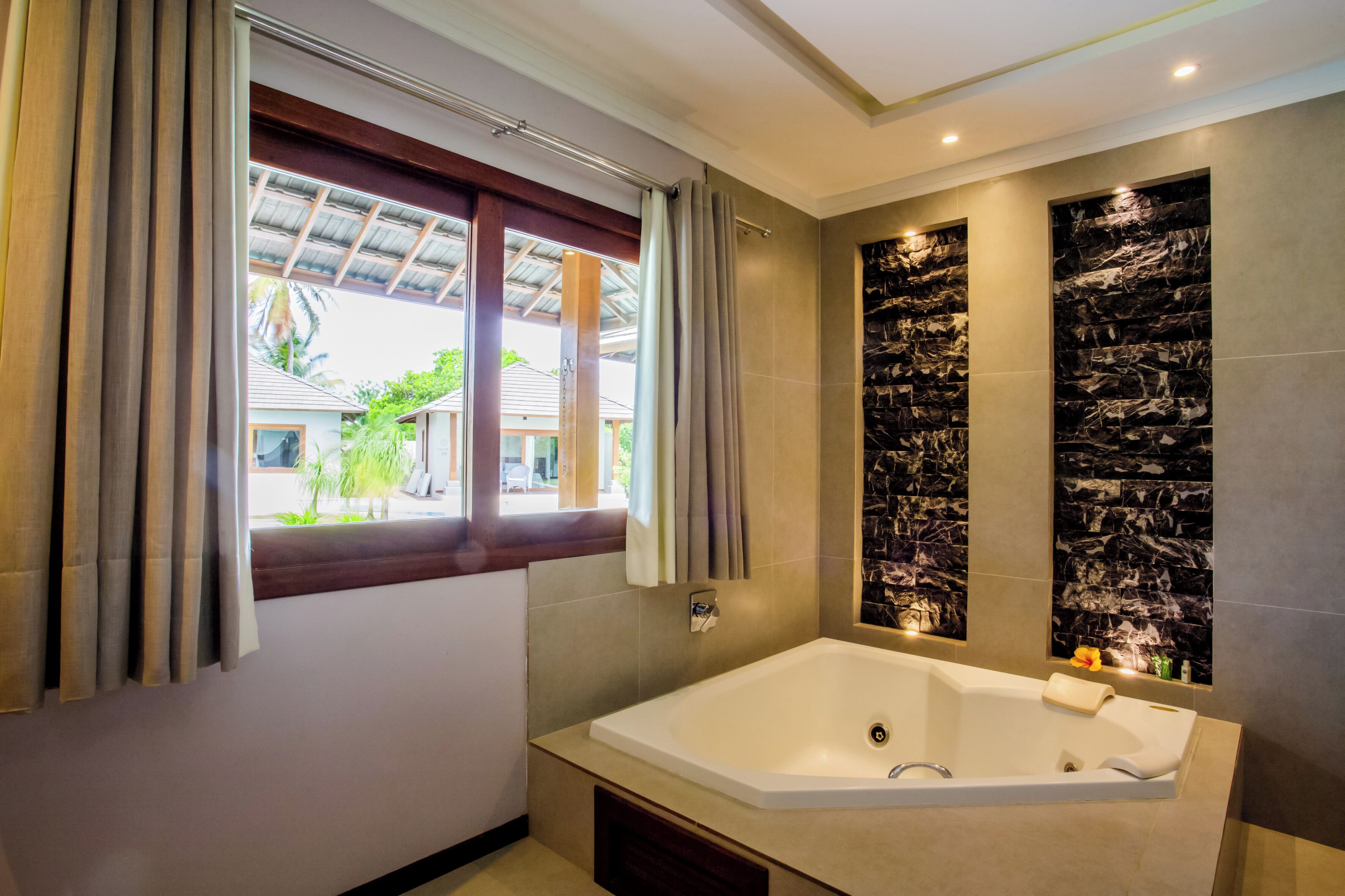 A modern bathroom with a large bathtub, a window with curtains, and a wall with a black and white marble design.