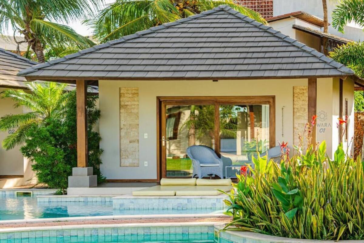 Un área de descanso junto a la piscina con un espacio de asientos cubierto, una entrada con puerta de cristal y una piscina con agua cristalina.