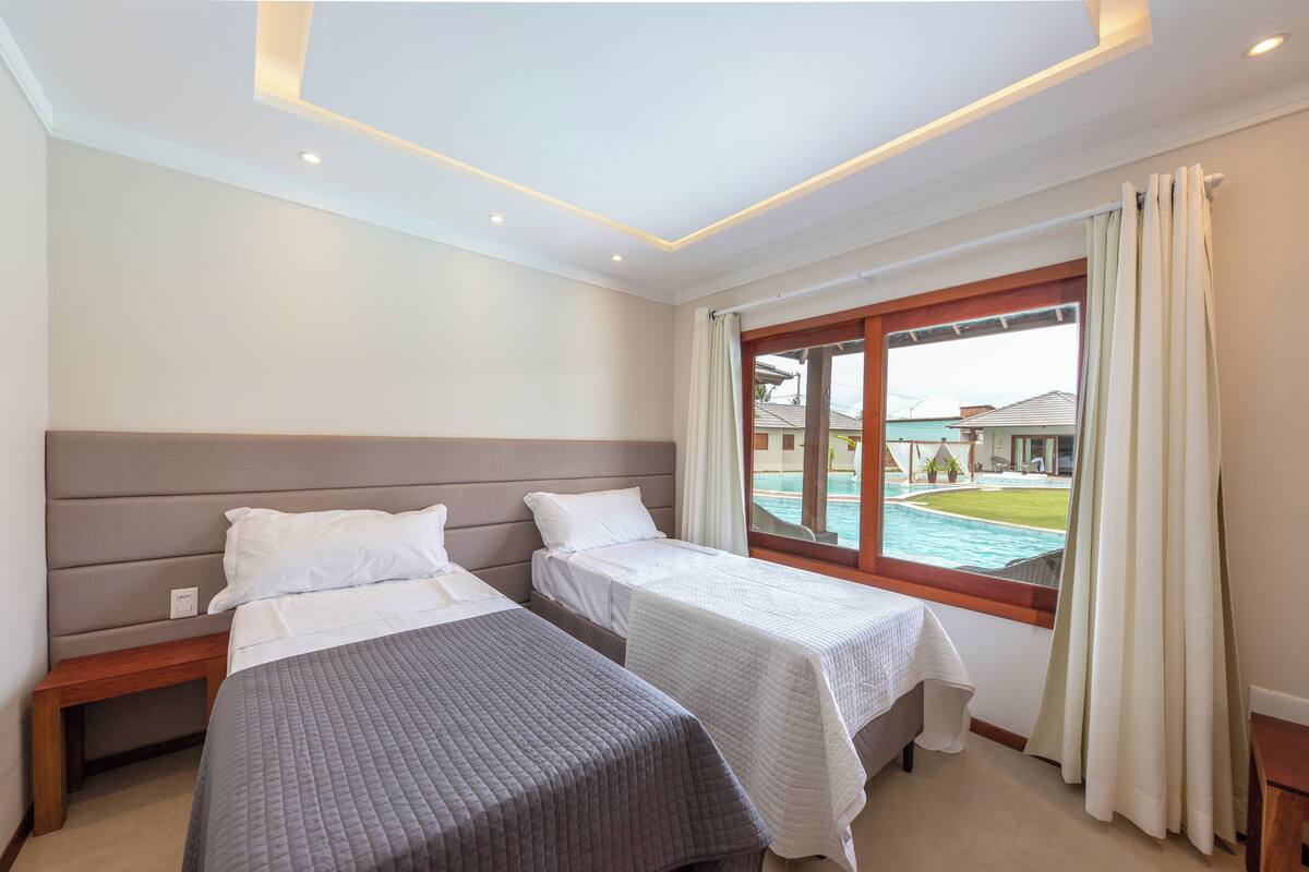 Habitación de hotel con dos camas individuales, una mesita de noche de madera, un ventanal con cortinas y vista a una piscina.
