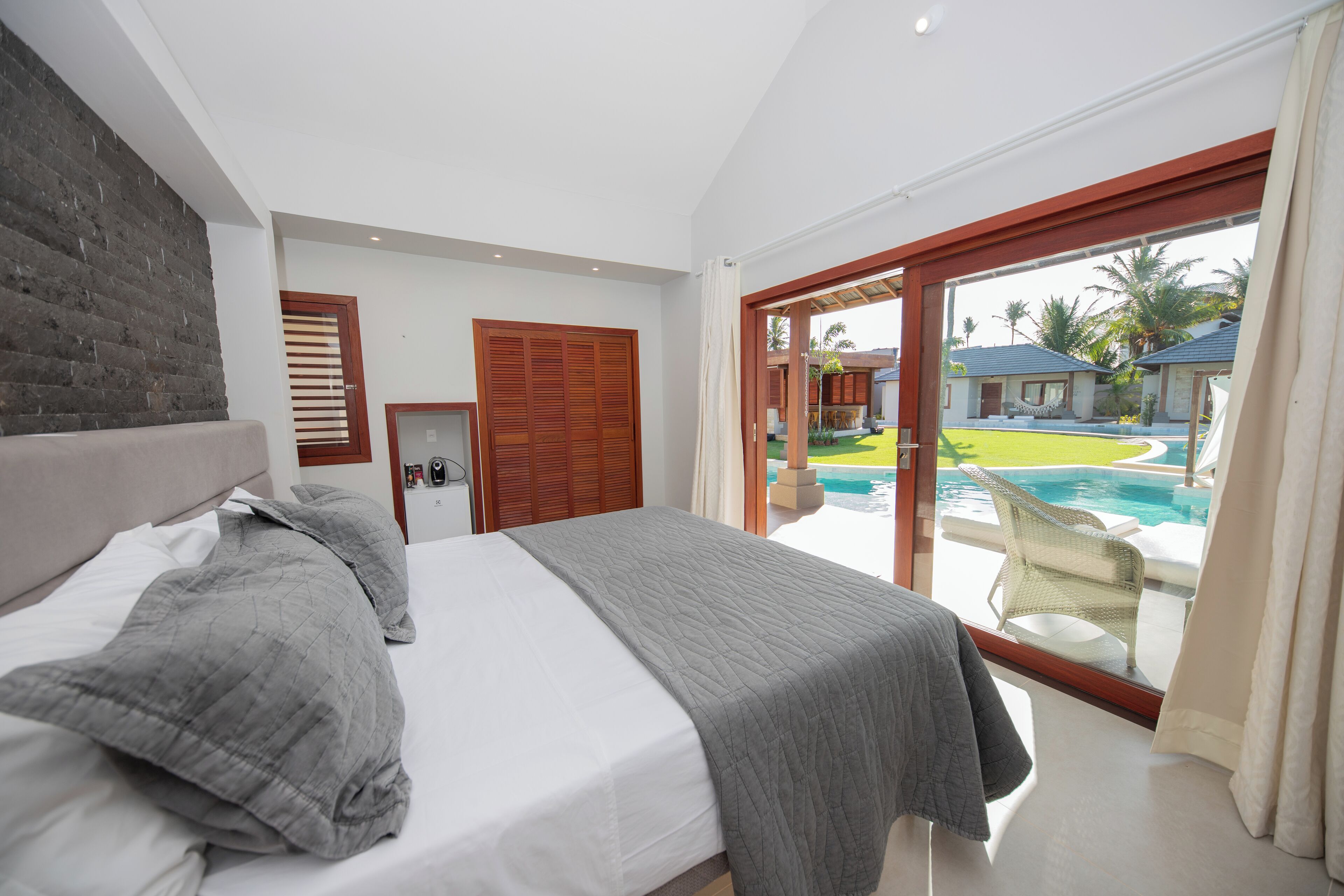 A bedroom with a bed, a wooden door, and a view of a swimming pool and outdoor seating.