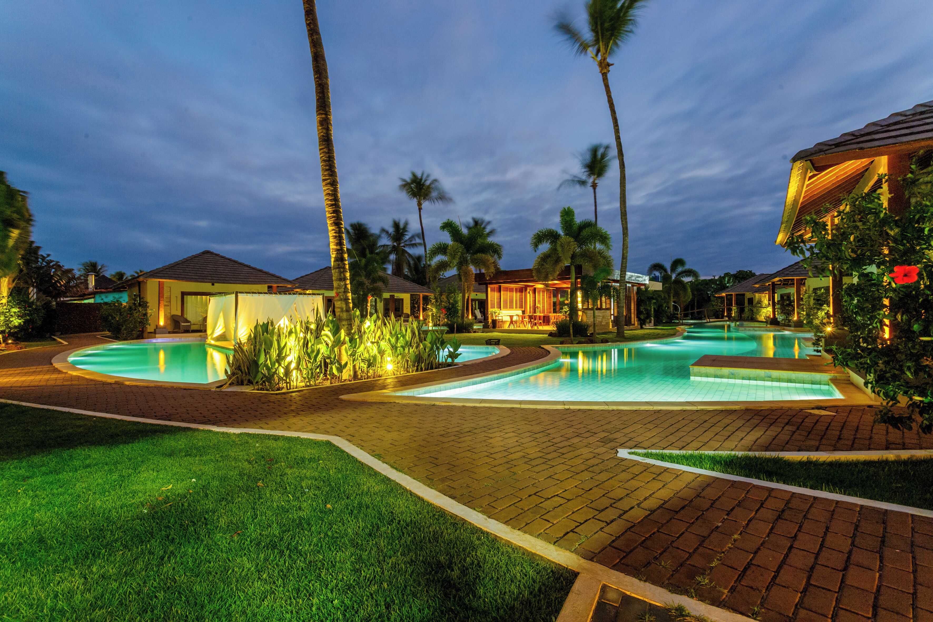 Un resort con dos piscinas, palmeras y senderos bien iluminados.