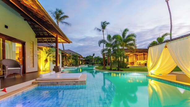 A swimming pool with tiled flooring, a covered seating area, and palm trees in the background. - Awara Pousada Boutique (São Miguel do Gostoso)