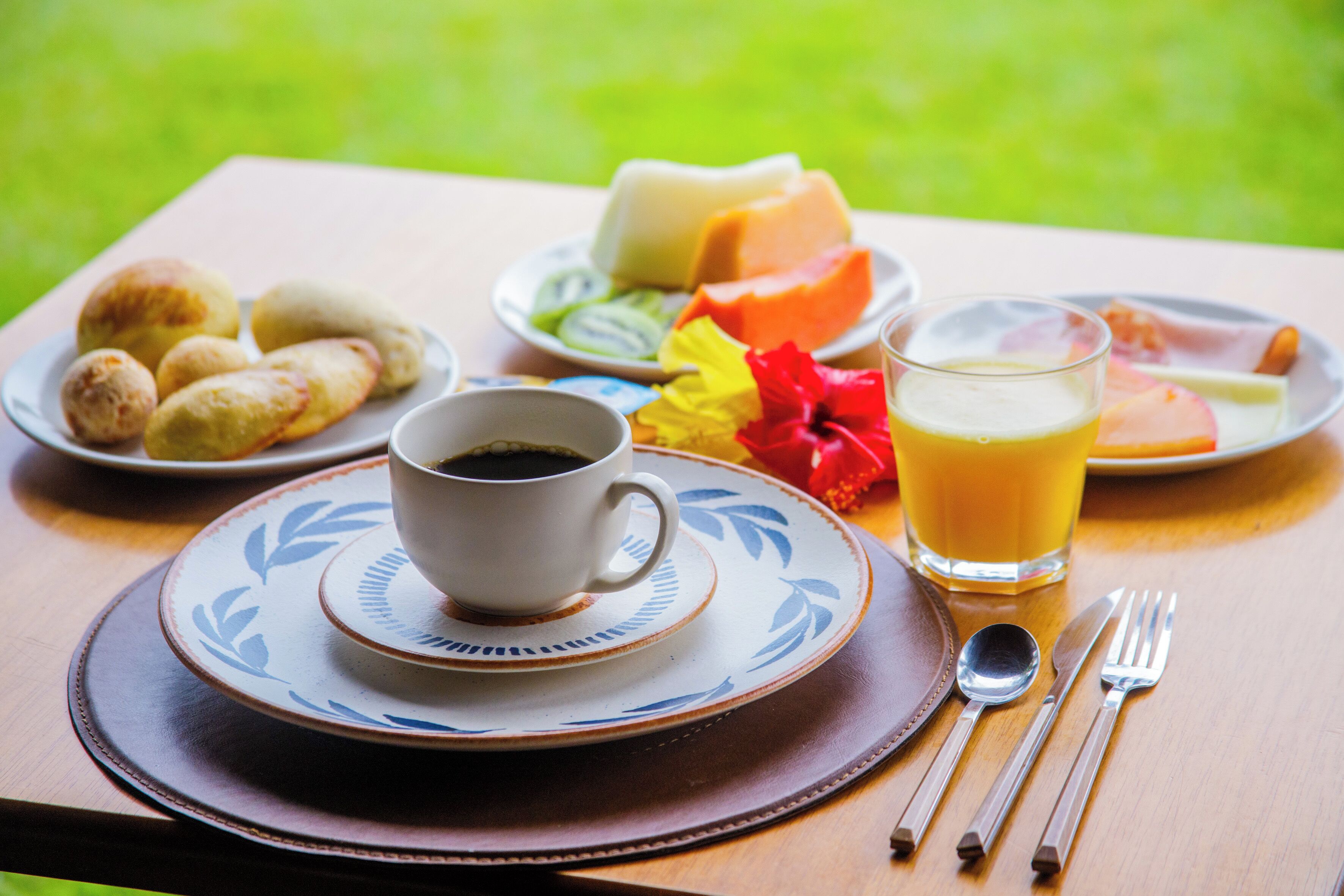 Una mesa de desayuno con una taza de café, un vaso de jugo de naranja y platos de comida que incluyen pan, queso y fruta.