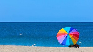 Escena de playa con una sombrilla colorida y un cielo azul despejado.