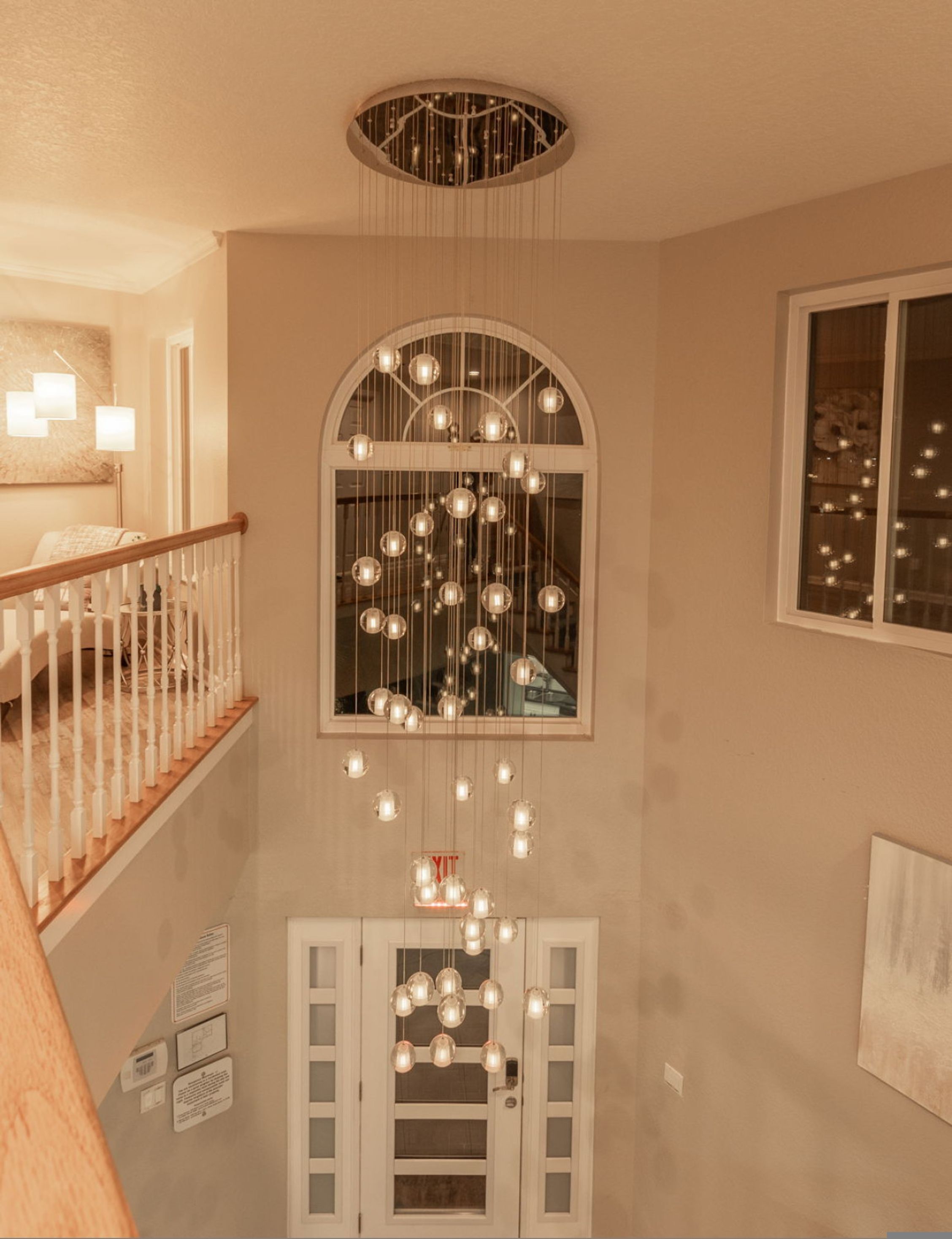 Un intérieur à plusieurs niveaux, avec un escalier, un luminaire décoratif au plafond et une fenêtre agrémentée de suspensions.