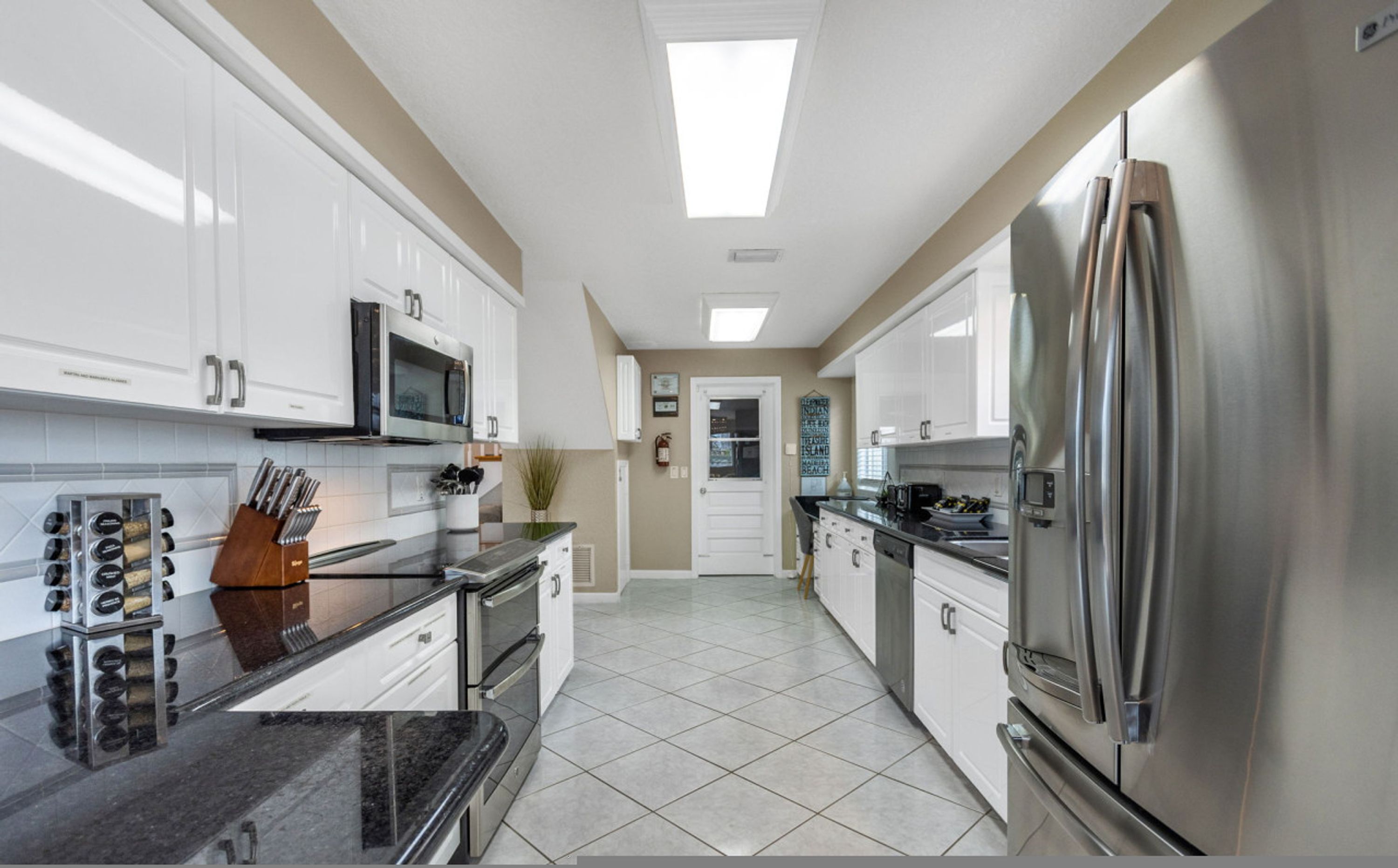 A modern kitchen with white cabinets, stainless steel appliances, and a tiled floor.