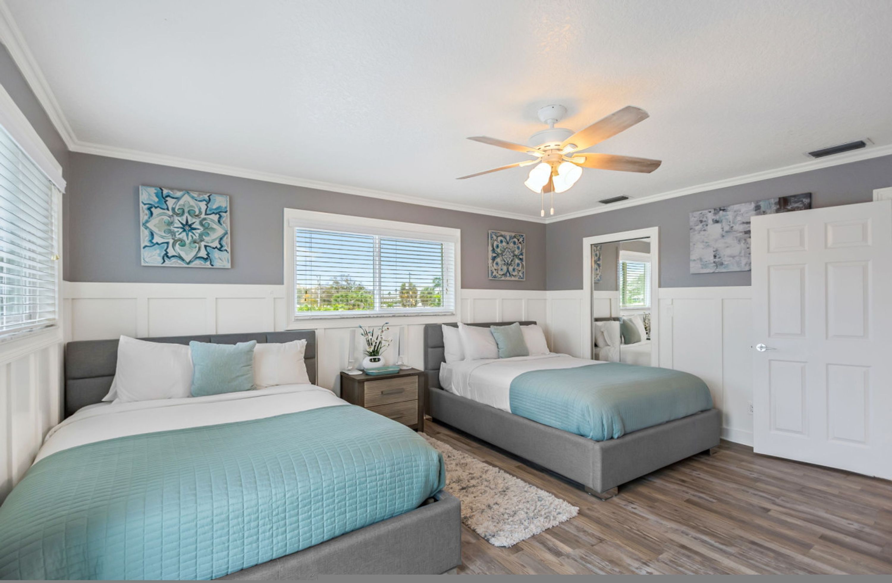 A bedroom with two beds, a ceiling fan, and artwork on the walls.