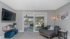 Een moderne woonkamer met een flatscreen televisie, een bank, een salontafel en een glazen schuifdeur die leidt naar een terras.