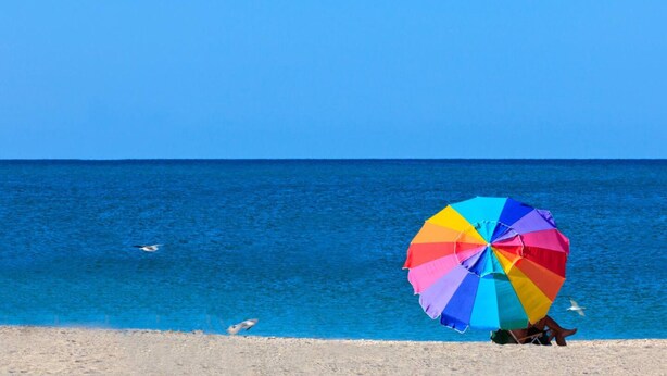 Een strandzicht met een kleurrijke parasol en een helderblauwe lucht.