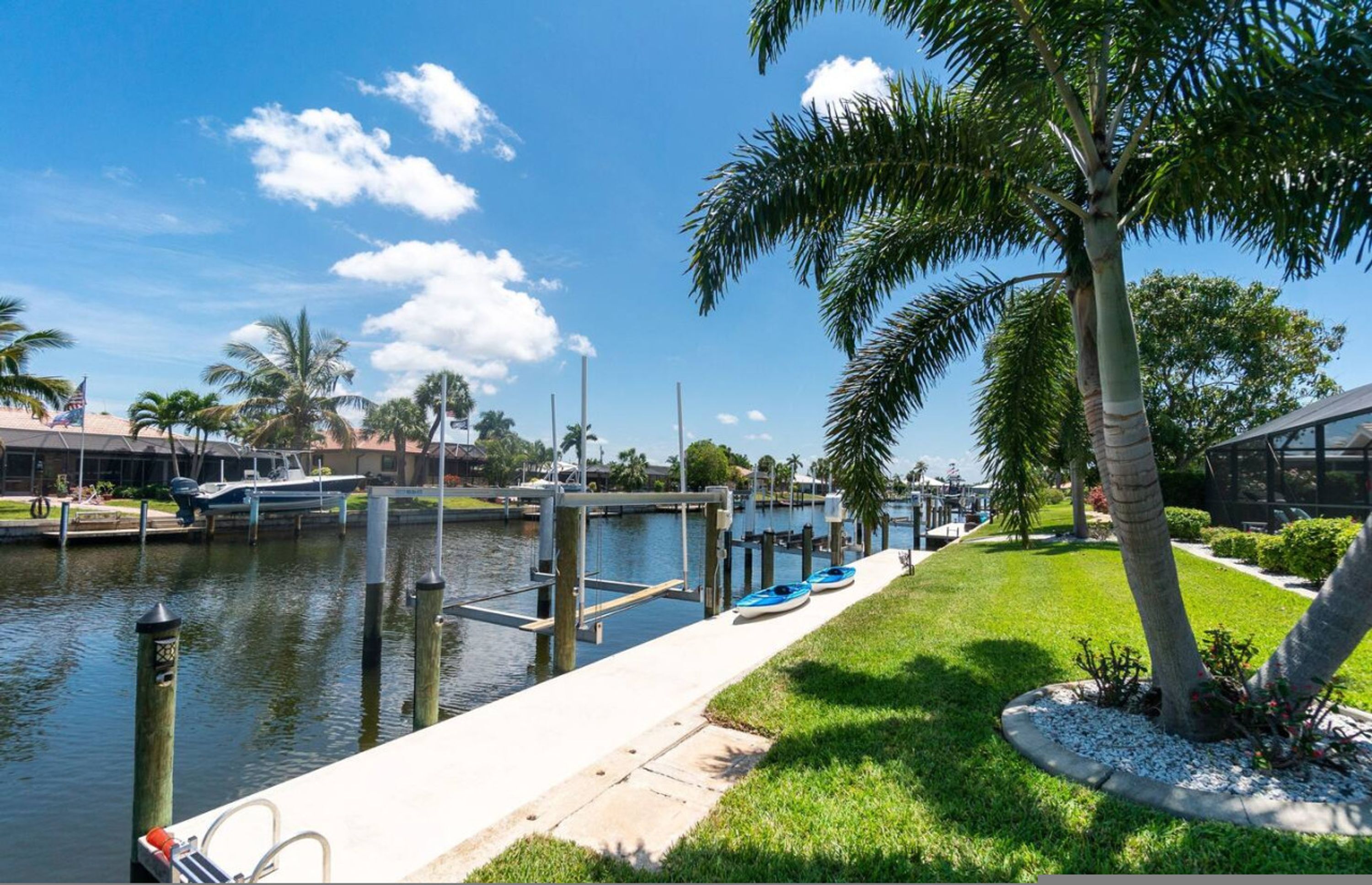 A marina with boats docked, a grassy walkway, and palm trees.